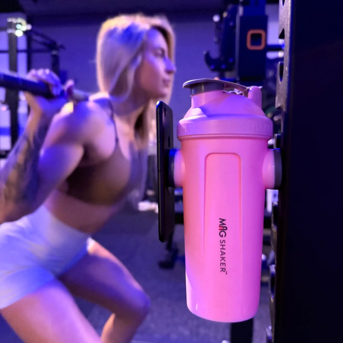 Fit female squatting with 28oz pink MagShaker bottle and phone mounted on squat rack